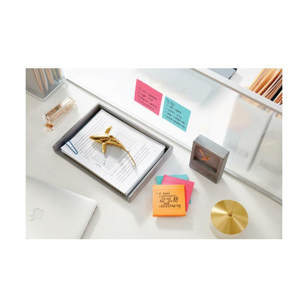 Desk scene with pink and aqua lined Post-it notes stuck to a glass shelf and an orange note pad beside a document tray