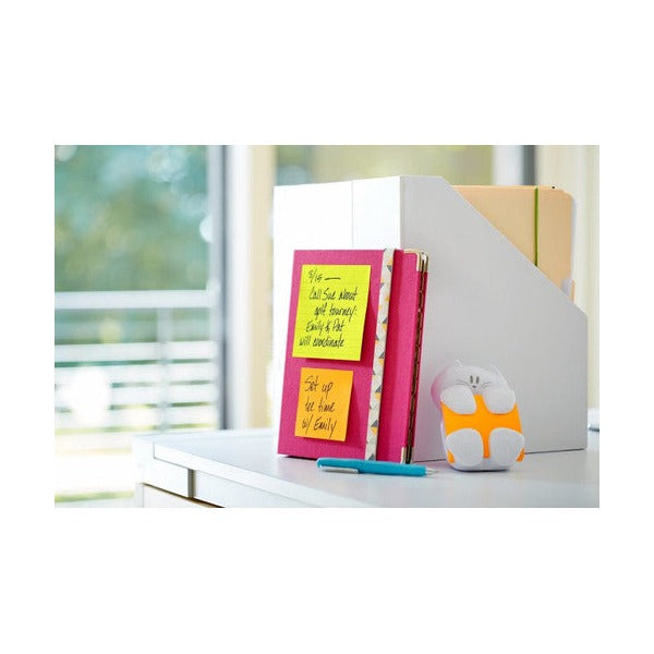 Pink and yellow Post-it notes with handwritten reminders stuck to a book on a desk stand