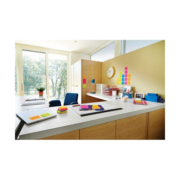 Corner office with a long white desk, coloured notes on the desk and a grid of sticky notes on the wall by a clock
