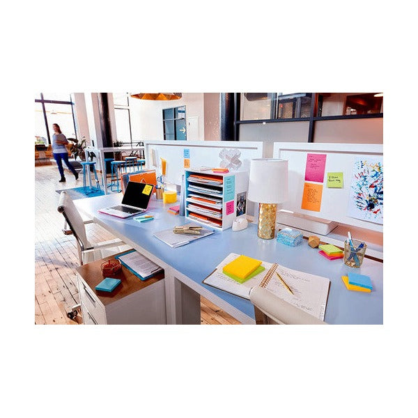 Bright open-plan office desk with a laptop, lamp and file sorter, coloured notes on the desk and screen