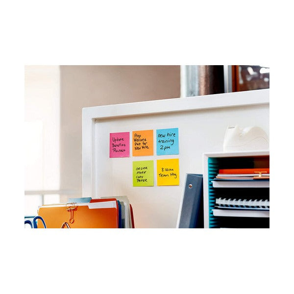 Coloured square notes with handwritten reminders arranged on a white partition next to a file sorter