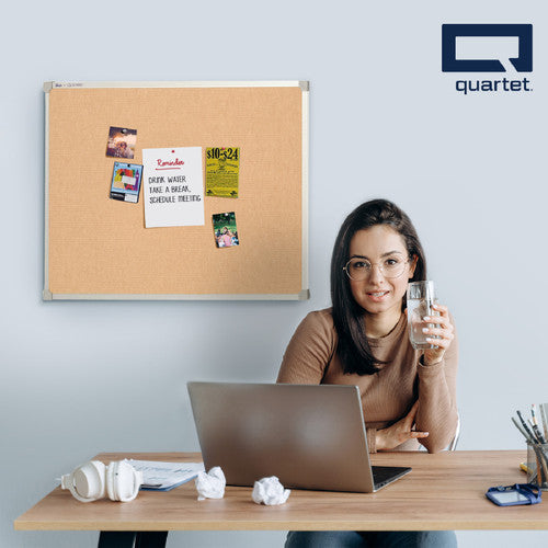 Quartet aluminium framed corkboard on an office wall above a desk, holding a reminder note, flyers and photos pinned to the cork