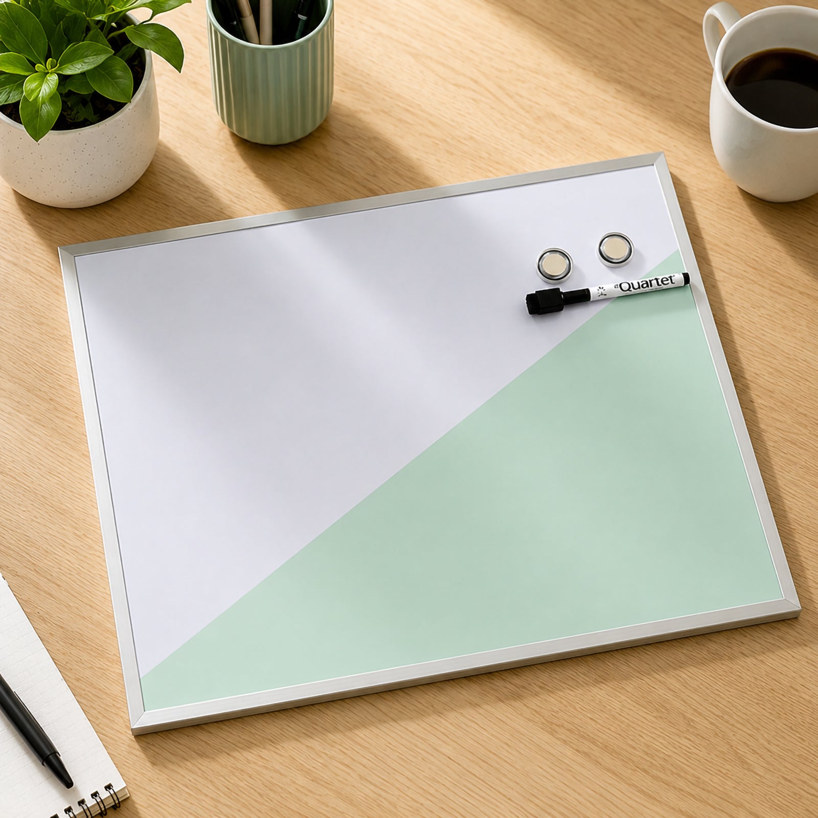 Top view of the Quartet Geo Magnetic Whiteboard Teal 430 x 580mm placed on a wooden desk alongside office stationery, plants and coffee. The clean magnetic writing surface with included magnets and marker highlights its modern appearance and everyday functionality.
