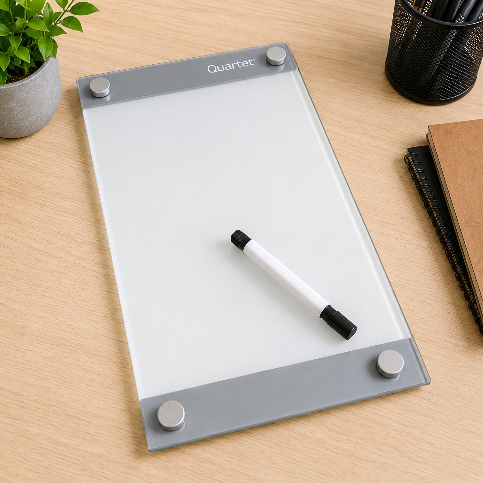 Top view of the Quartet Infinity Custom Glassboard 279 x 432mm placed on a timber desk with the included dry erase marker. The elegant frameless magnetic glassboard is shown alongside office accessories, highlighting its premium construction and customisable design.