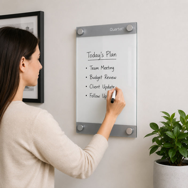 Quartet Infinity Custom Glassboard 279 x 432mm mounted on a modern office wall while a professional writes a daily task list using the premium magnetic glass surface. The frameless floating design creates a clean contemporary appearance that is ideal for home offices, executive workspaces and meeting rooms.