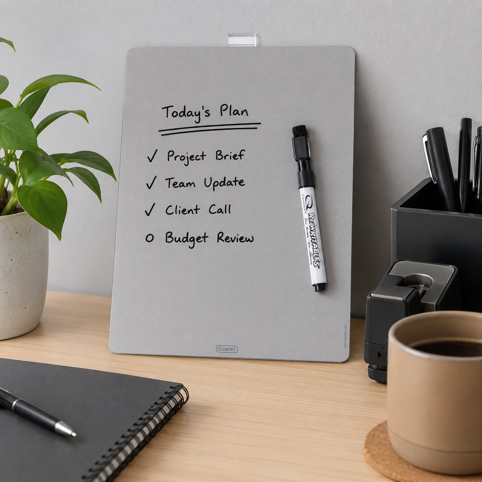 The Quartet Magnetic Whiteboard Tile Silver 216 x 280mm displayed in a modern workspace featuring a completed daily planner. The reusable dry erase board is paired with the included marker and blends naturally into a contemporary office environment.