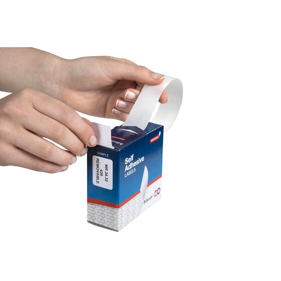 Hands pulling a white 24 x 32mm removable label out through the slot of a QuikStik dispenser box