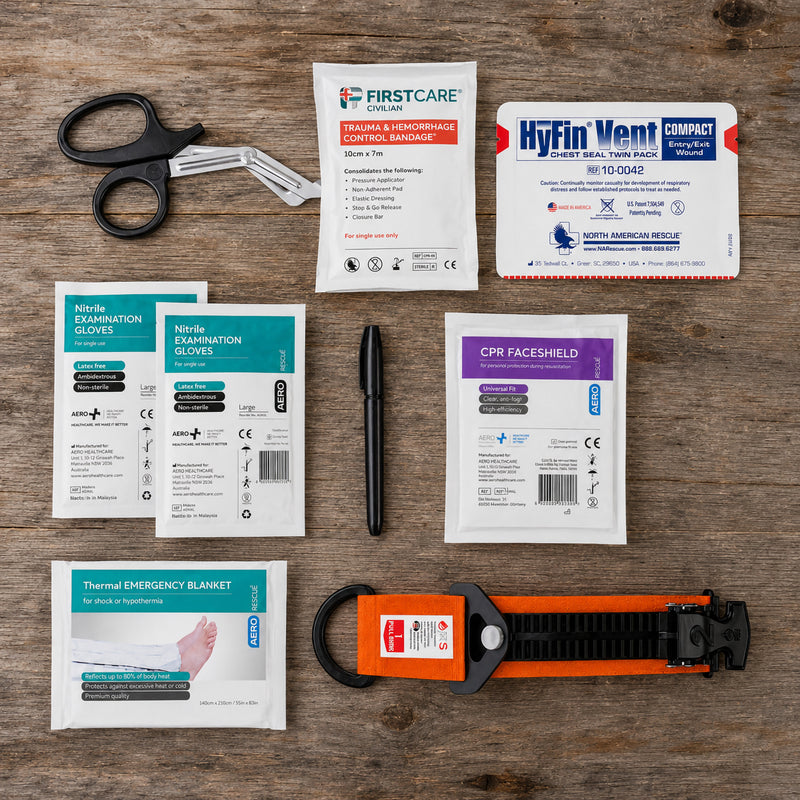 Contents of the RapidStop Medium bleeding control kit arranged neatly on a timber surface. Visible components include the orange RapidStop tourniquet, trauma and haemorrhage control bandage, HyFin Vent Compact Chest Seal Twin Pack, thermal emergency blanket, CPR faceshield, two nitrile glove packs, trauma shears and black marker.