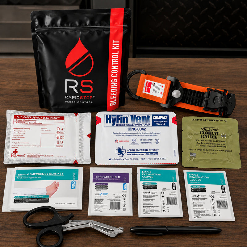 RapidStop Medium trauma kit presented with its black bleeding control pouch and orange RapidStop tourniquet in an emergency equipment setting. The layout clearly displays the QuikClot Combat Gauze alongside the chest seal twin pack, emergency bandage, thermal blanket, CPR faceshield, two glove packs, trauma shears and treatment marker.