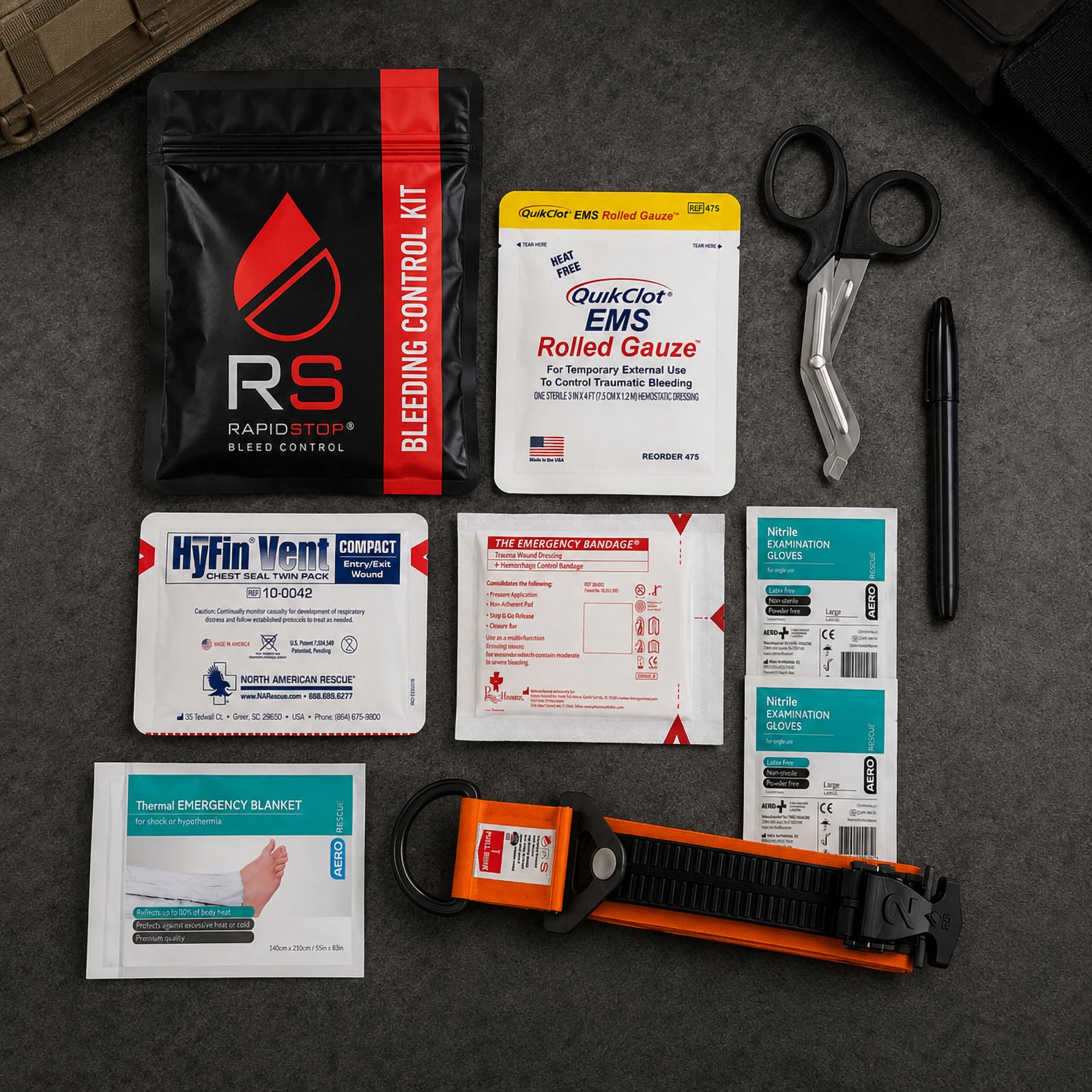 Complete RapidStop Medium Bleed Control Kit arranged on a dark surface for a clear overview of the contents. Visible equipment includes the RapidStop tourniquet, QuikClot EMS Rolled Gauze, HyFin Vent Compact chest seal twin pack, emergency trauma bandage, thermal emergency blanket, nitrile examination gloves, trauma shears, marker and black RapidStop kit pouch.