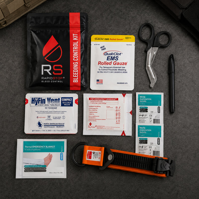 Complete RapidStop Medium Bleed Control Kit arranged on a dark surface for a clear overview of the contents. Visible equipment includes the RapidStop tourniquet, QuikClot EMS Rolled Gauze, HyFin Vent Compact chest seal twin pack, emergency trauma bandage, thermal emergency blanket, nitrile examination gloves, trauma shears, marker and black RapidStop kit pouch.