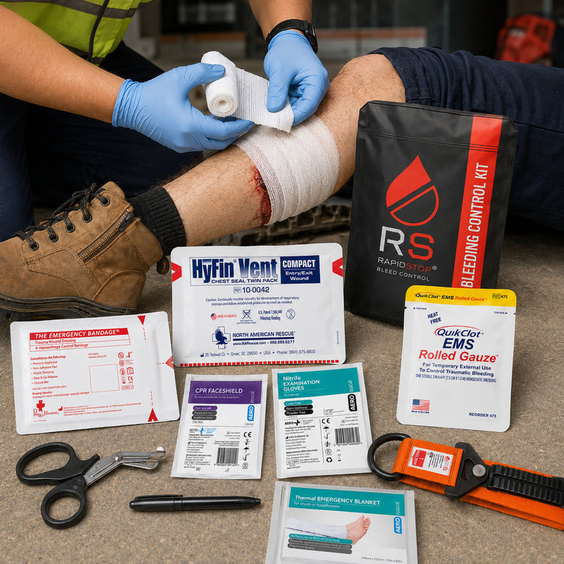 RapidStop Bleed Control Medium Pack shown during a simulated workplace trauma response as a gloved responder applies rolled gauze to a leg injury. Surrounding equipment includes QuikClot EMS Rolled Gauze, RapidStop tourniquet, HyFin Vent Compact chest seal, emergency bandage, nitrile gloves, CPR faceshield, thermal blanket, trauma shears, marker and RapidStop pouch.