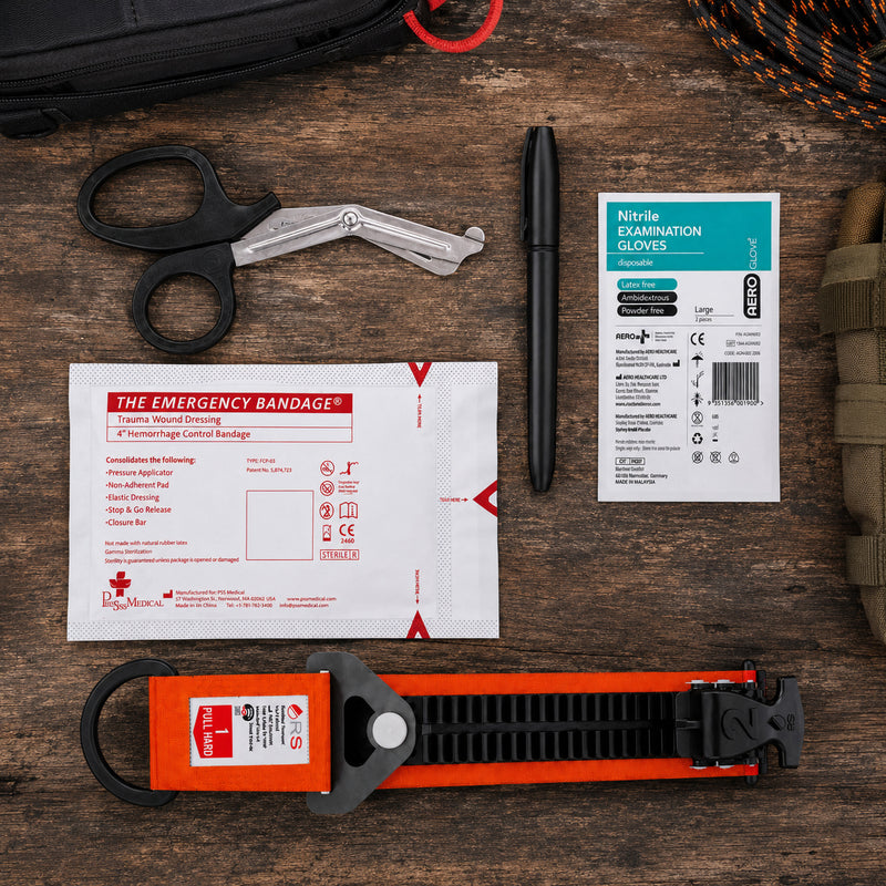 Contents of the RapidStop Small Bleed Control Pack arranged on a timber surface. The image clearly shows the orange RapidStop tourniquet, 4 inch emergency trauma bandage, trauma shears, disposable nitrile examination gloves and black marker, highlighting the focused selection of essential equipment supplied in the RSK401 configuration.