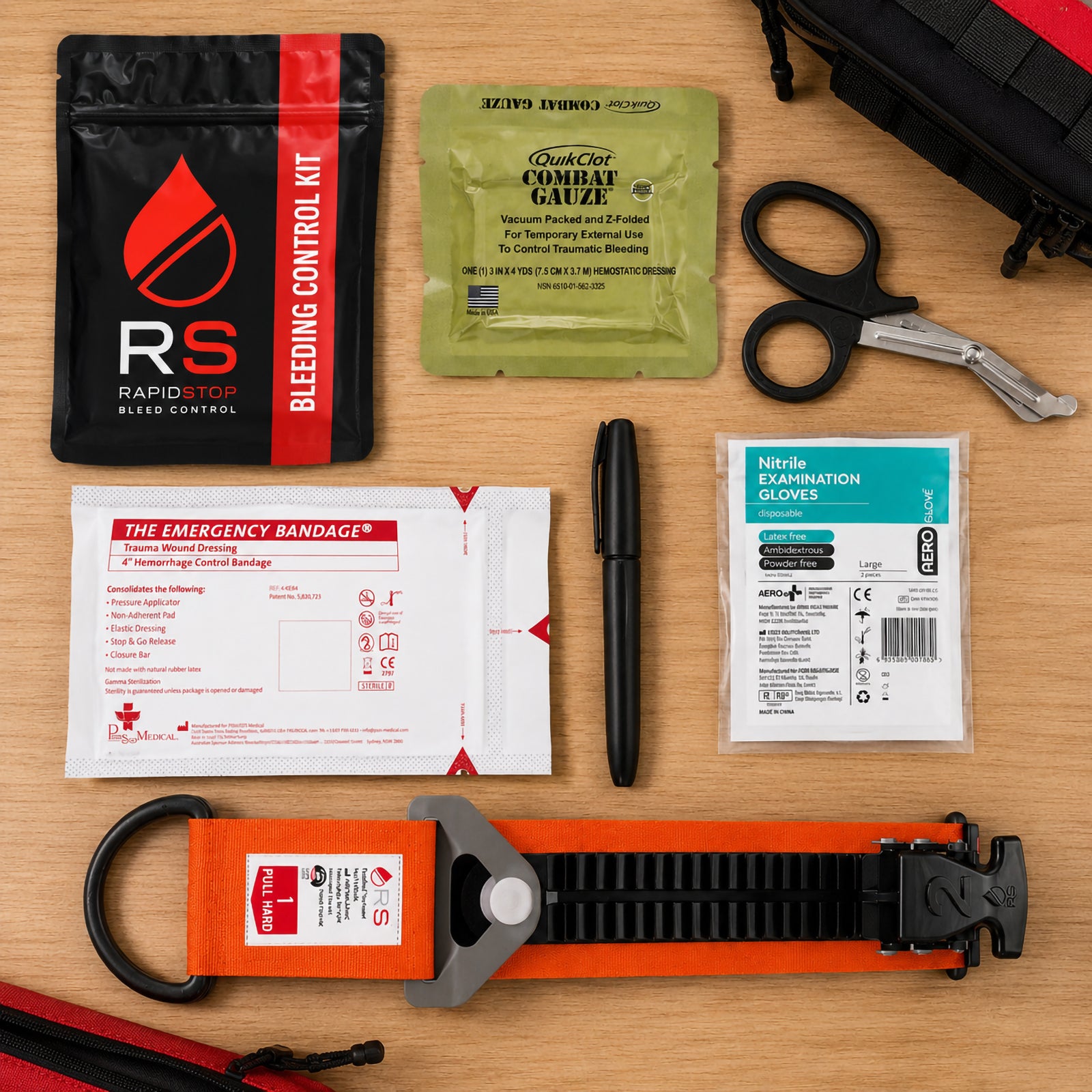 RapidStop Bleed Control Small Pack contents arranged neatly on a timber surface, including the black and red RapidStop pouch, QuikClot Combat Gauze, trauma shears, 4 inch emergency haemorrhage control bandage, nitrile examination gloves, marker and orange RapidStop tourniquet.