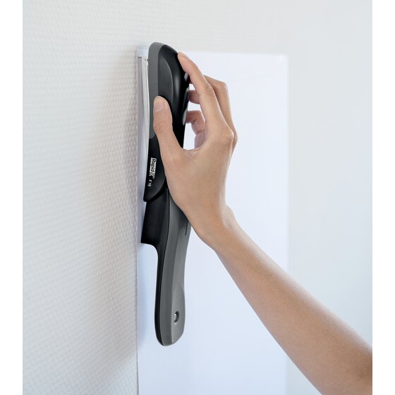 Hand pressing an opened out black Rapid F16 stapler against a wall to pin a sheet of paper
