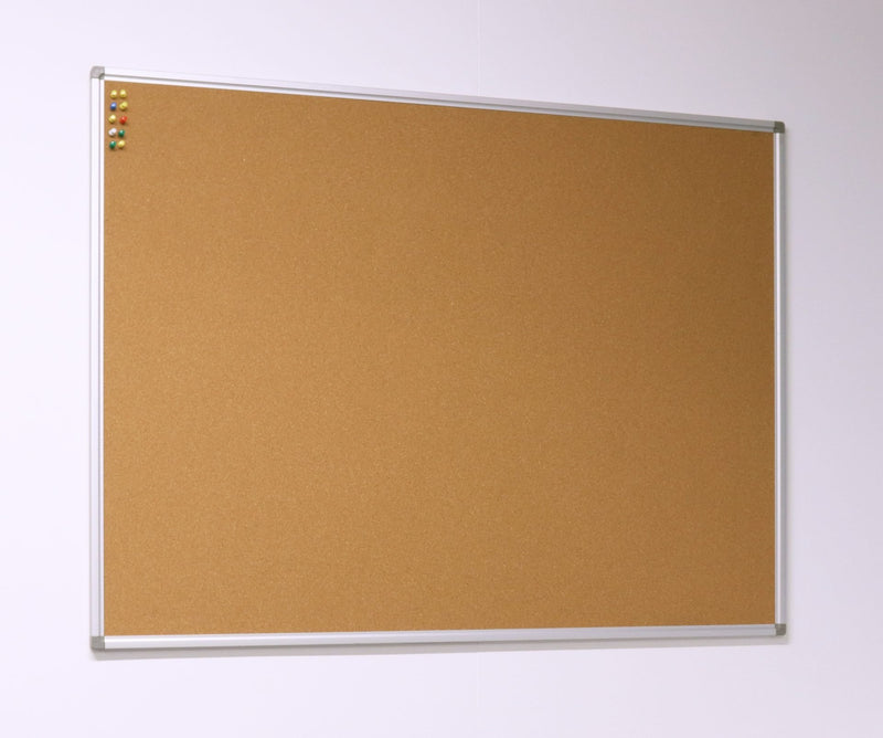 Rapidline Standard Corkboard hung on a pale wall and seen from an angle, with an aluminium frame and pins clustered in the top left corner.