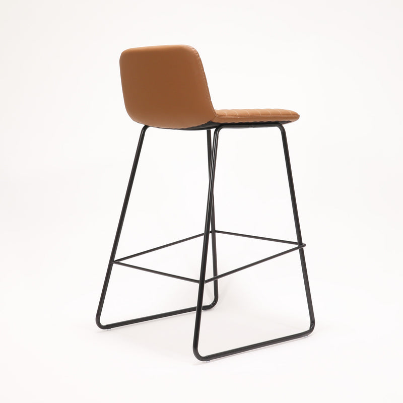 Rapidline Pixel bar high stool in amber PU on a black powdercoated tall sled base with a foot rail, product photograph on a plain background showing the ribbed horizontal stitching across the seat and back.
