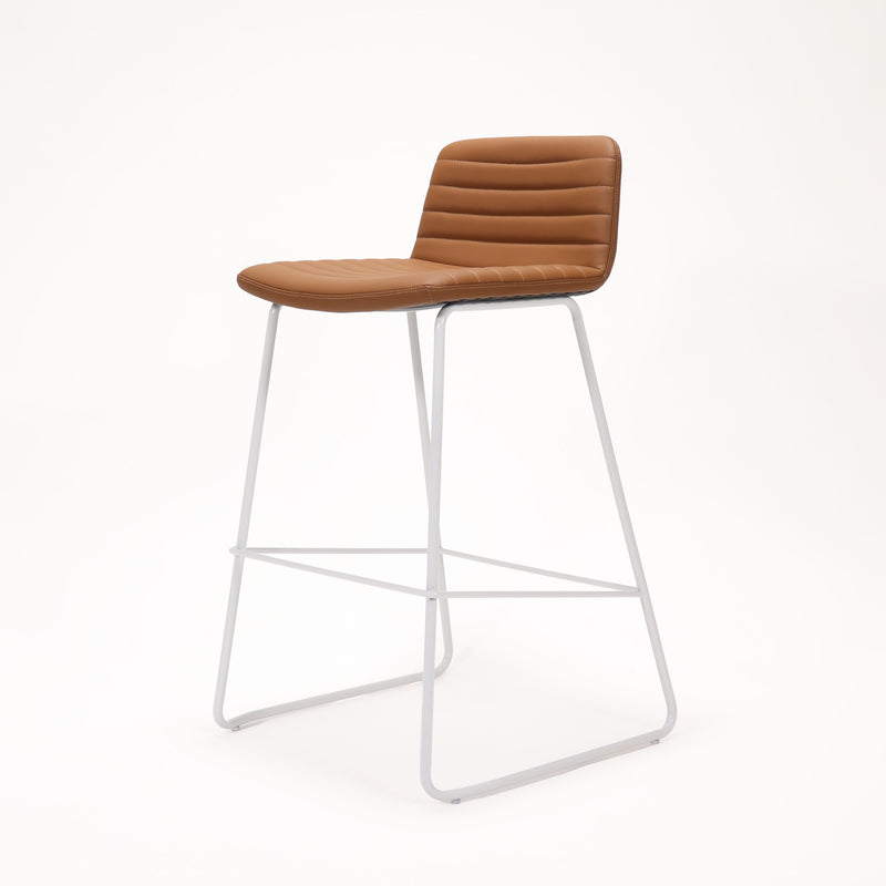 Rapidline Pixel bar high stool in amber PU on a white powdercoated tall sled base with a foot rail, product photograph on a plain background showing the ribbed horizontal stitching across the seat and back.