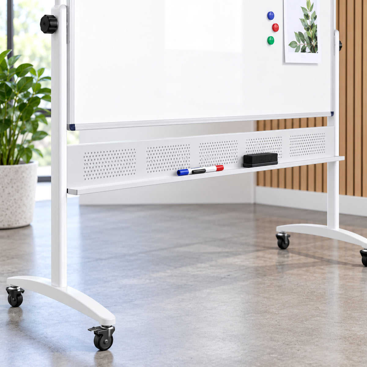 Close up lifestyle view of the Rapidline 1500 x 1200mm mobile magnetic whiteboard showing the lower aluminium frame, full width pen tray, perforated support panel and castor equipped mobile base. Whiteboard markers and an eraser are stored within easy reach, while magnets and a displayed reference sheet demonstrate the practical magnetic surface.