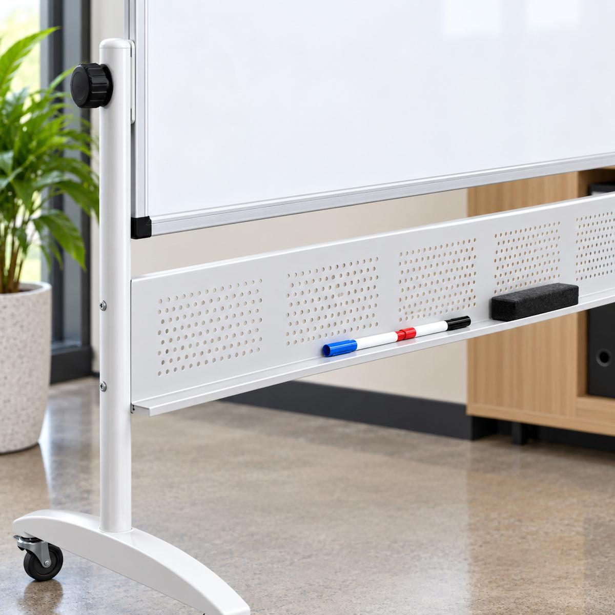 Close up view of the Rapidline 1800 x 1200mm mobile magnetic whiteboard showing the aluminium board edge, pivot adjustment control, perforated support panel and integrated pen tray. Whiteboard markers and an eraser are positioned on the tray, highlighting convenient accessory storage and the practical construction of the heavy duty mobile stand.
