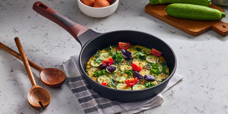 A Resto Capella frypan holding a zucchini and tomato frittata, showing the 3D-textured exterior and wood-grain handle (Resto lifestyle image)
