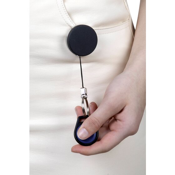 Rexel heavy duty key reel worn in use, the black reel clipped to a cream top with the cord drawn down to a hand holding a blue oval fob.