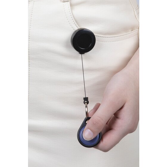 Rexel mini key reel worn in use, the small black reel clipped to a cream top with the cord pulled down to a hand holding a blue oval fob.