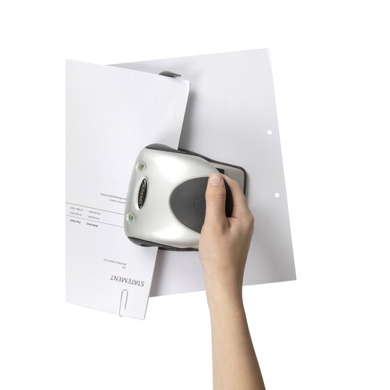 A hand pressing the Rexel Precision P240 2 hole punch down on a stack of white A4 statements, with two punched holes visible on the sheet behind