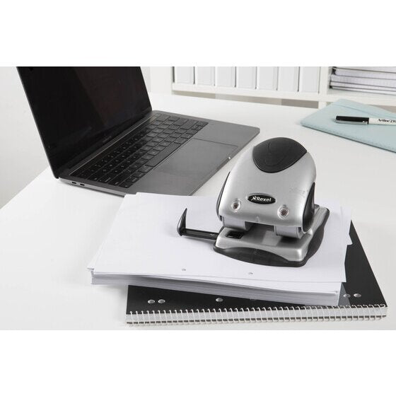 Rexel Precision P240 2 hole punch in use on an office desk beside a laptop, a thick stack of white paper and a spiral bound notebook