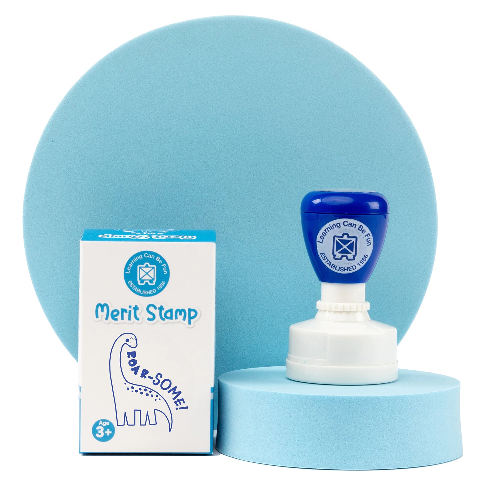 Retail packaging and Roar-some Merit Stamp displayed on a presentation stand with coordinated blue background elements. The self inking classroom stamp combines durability, convenience and motivation to help teachers reward positive learning outcomes.