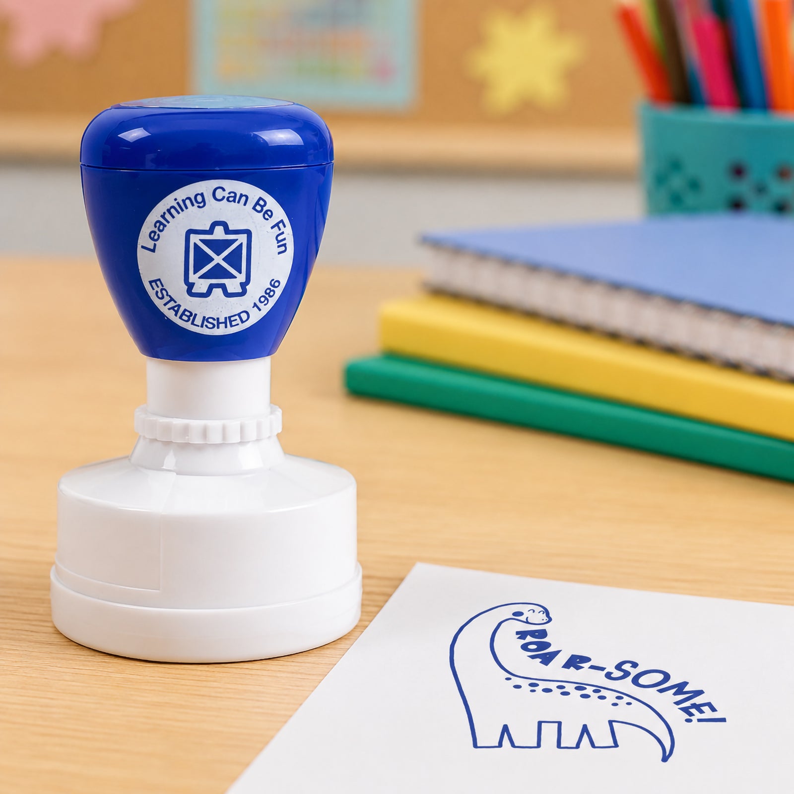 Close up classroom scene featuring the Roar-some reward stamp and dinosaur themed impression on paper. The vibrant blue stamp design stands out clearly, providing memorable recognition for outstanding work and participation.