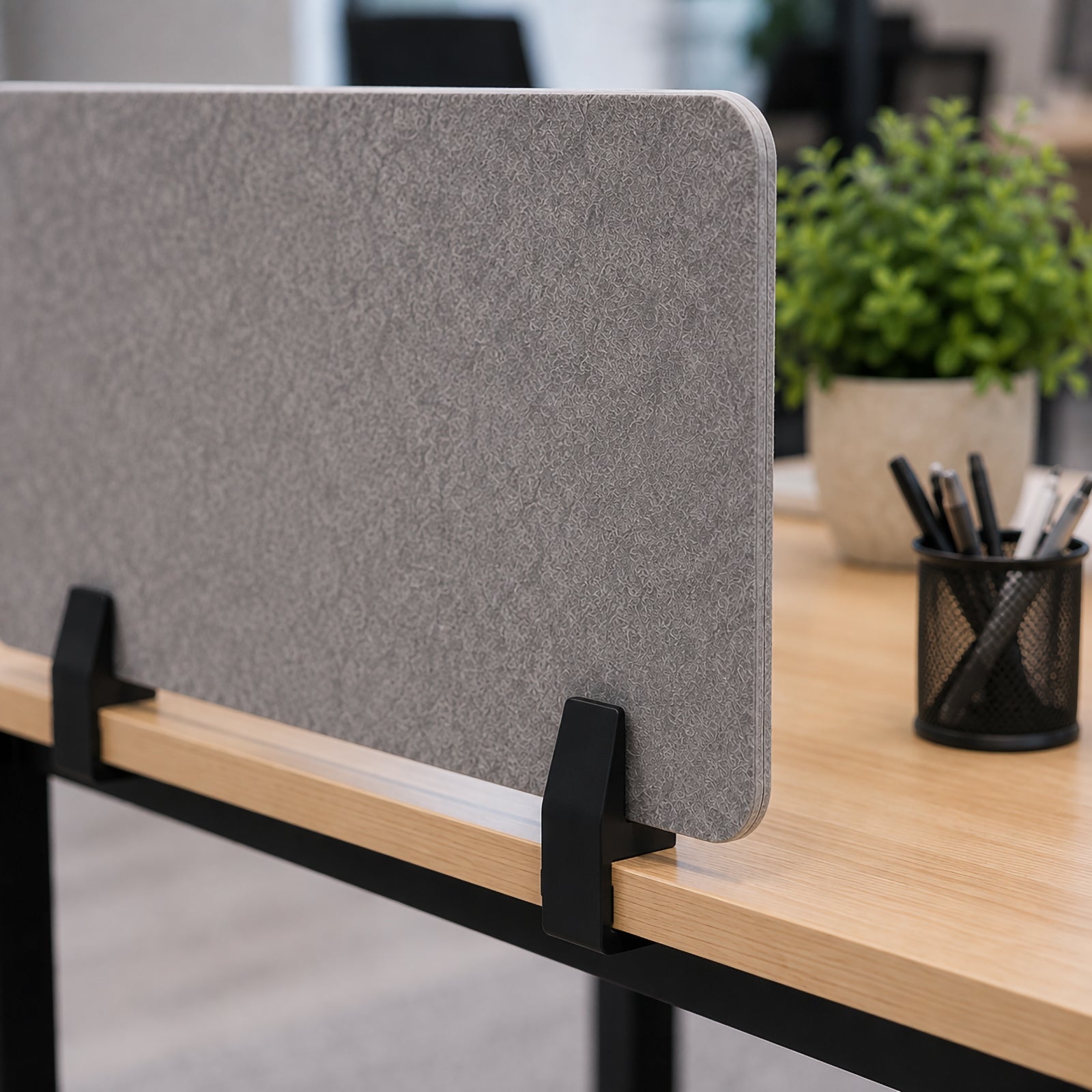 Close up view of two matte black SANA Type 2 undermount clamps holding a grey PET desk screen along the edge of a timber desktop, showing the discreet side mounting position and clean professional finish.