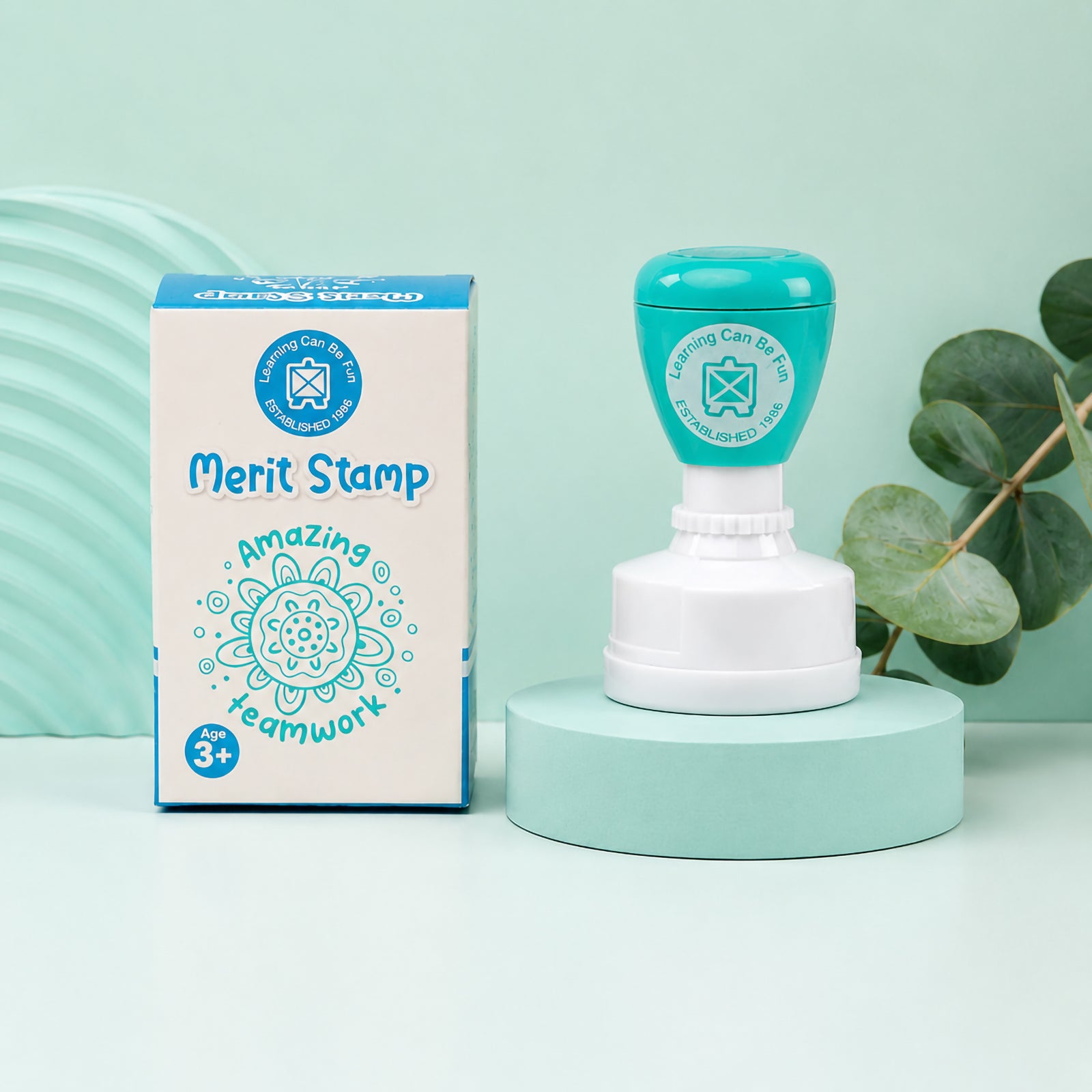 Retail packaging and the merit stamp are displayed together against a soft green backdrop. The image highlights the Sacred Country collection artwork, the Amazing Teamwork message and the attractive presentation ideal for classroom reward systems.