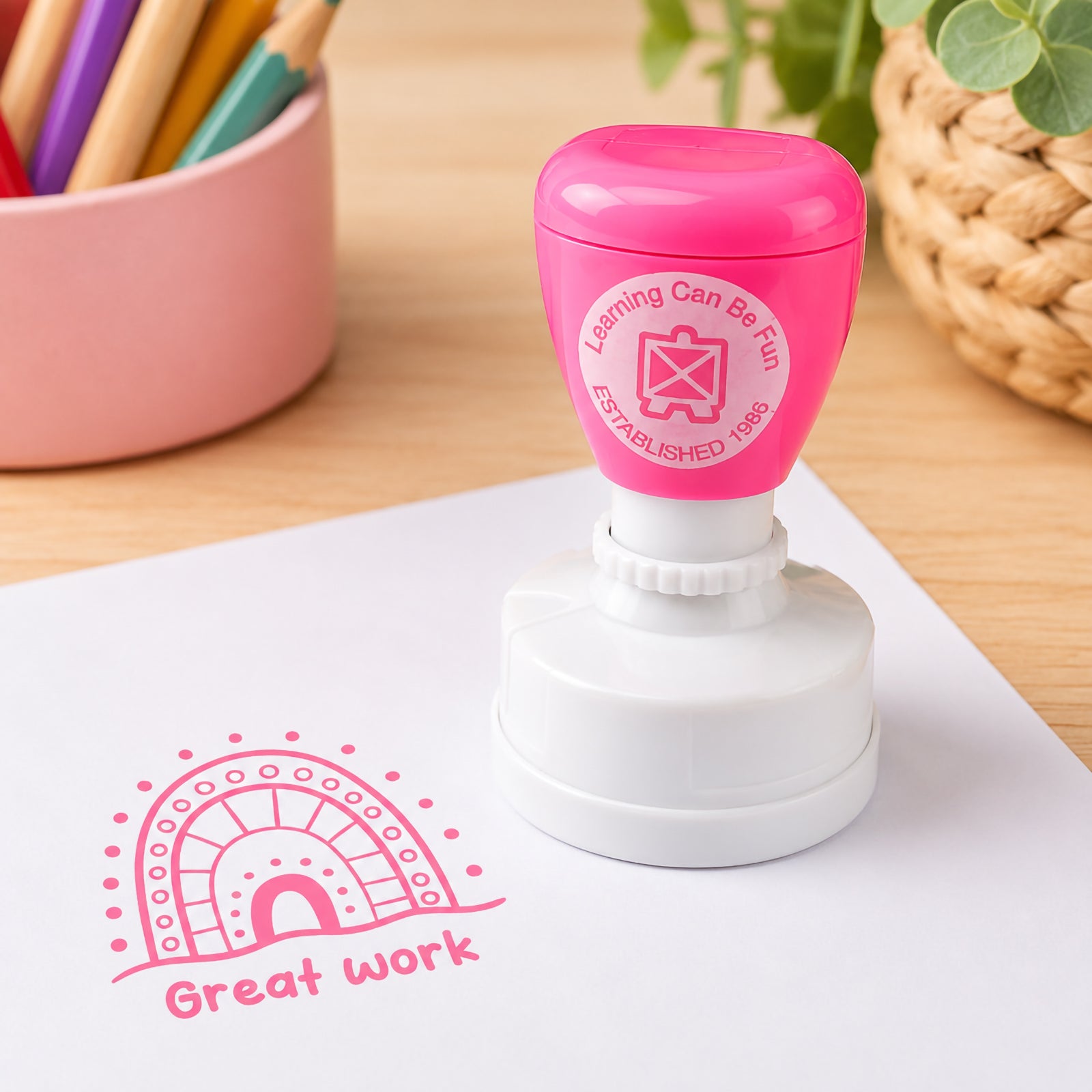 The merit stamp is displayed beside a crisp Great Work impression on white paper. Surrounded by classroom stationery and natural textures, the image showcases the stamp's clear detail, vibrant ink colour and suitability for everyday educational feedback.