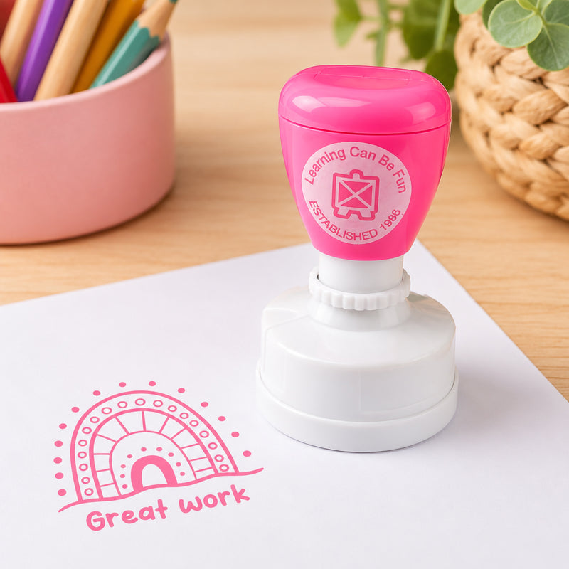 The merit stamp is displayed beside a crisp Great Work impression on white paper. Surrounded by classroom stationery and natural textures, the image showcases the stamp's clear detail, vibrant ink colour and suitability for everyday educational feedback.