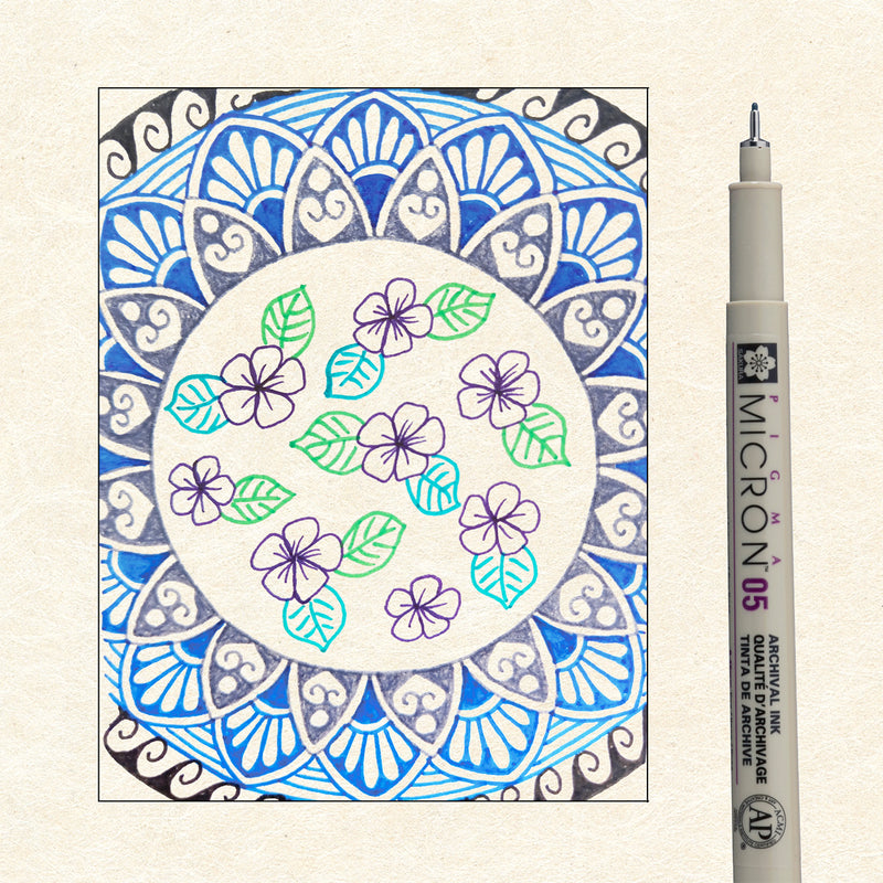 Sakura Pigma Mandala Cool Tone Set 05: blue mandala with purple flowers and green leaves drawn in Pigma ink beside a single Micron 05 pen