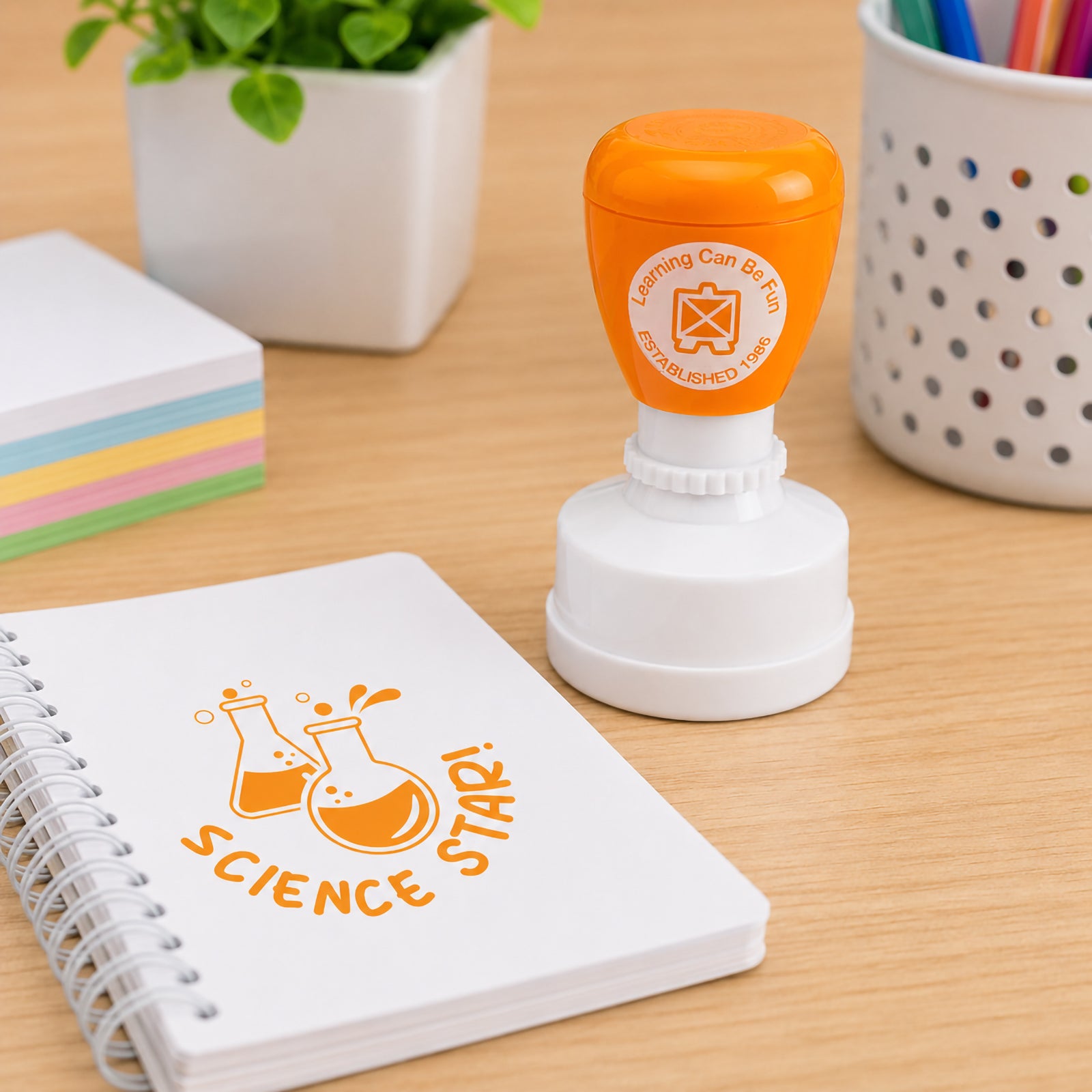 Science Star self inking merit stamp positioned next to a spiral notebook and colourful stationery. The bold orange impression highlights scientific learning and provides an engaging way for teachers to recognise effort, curiosity and academic progress.