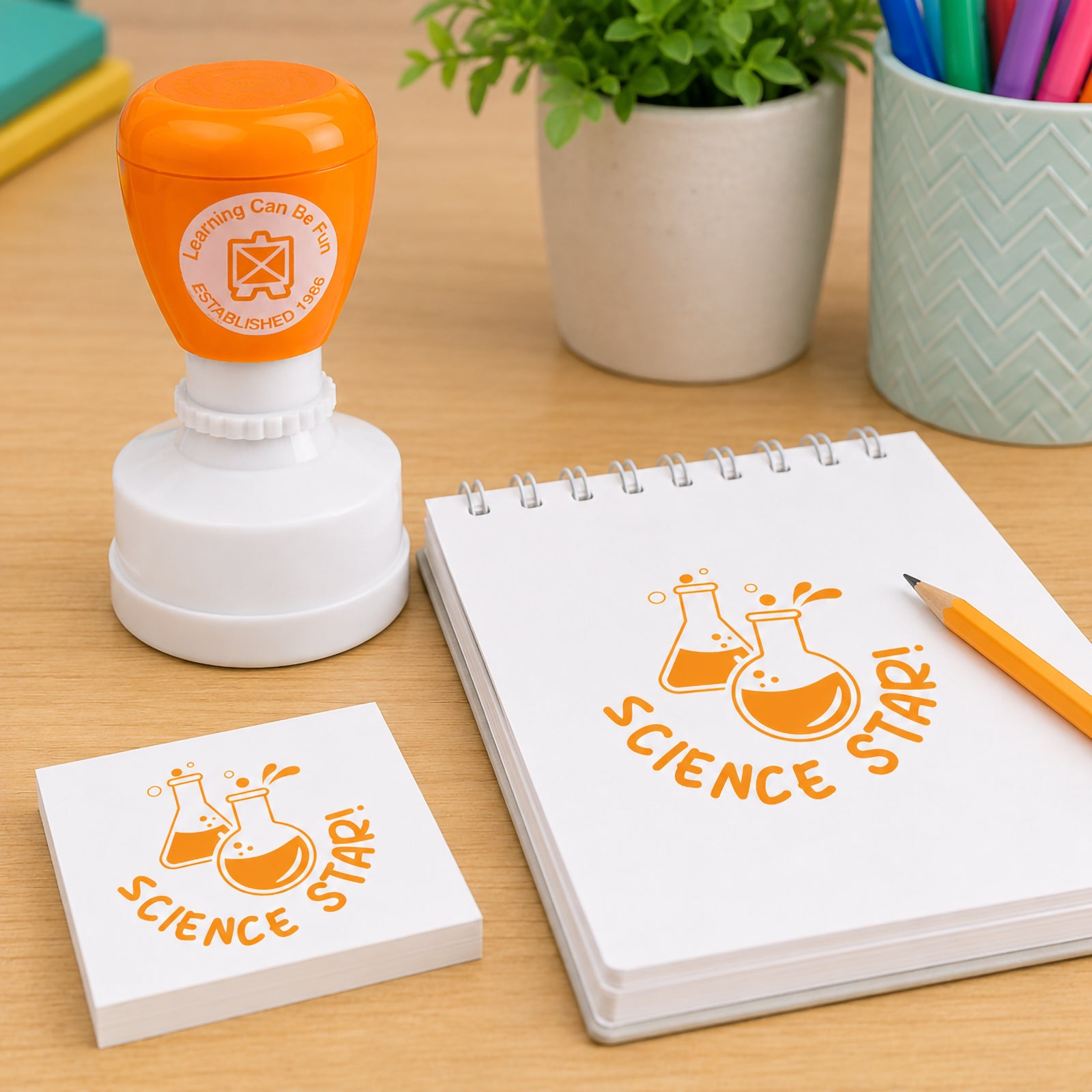 Learning Can Be Fun Science Star Merit Stamp displayed beside a notebook and pencil on a classroom desk. The self inking stamp creates a bright orange science themed impression featuring laboratory flasks and the Science Star message, making it ideal for rewarding STEM achievements and classroom success.