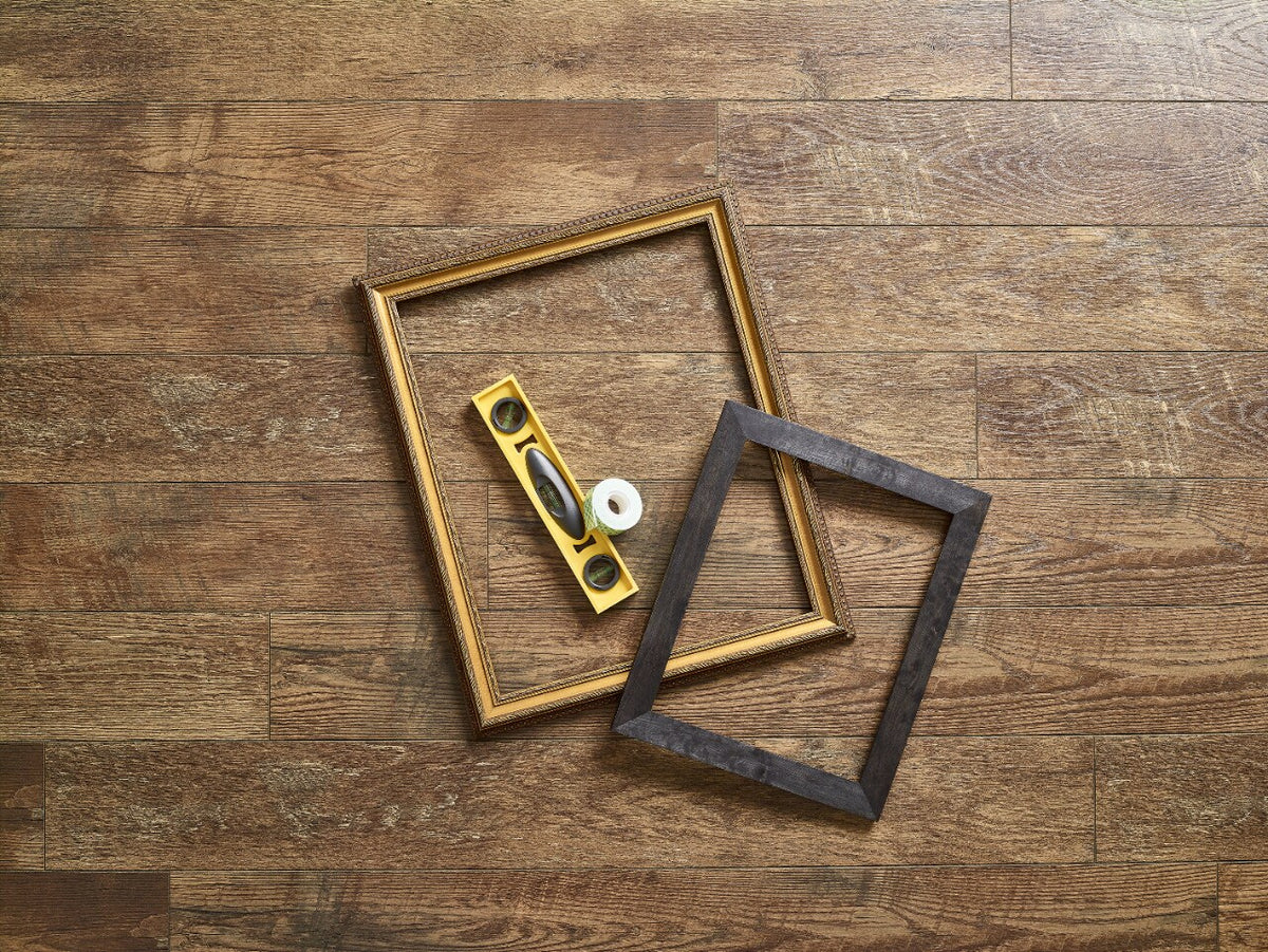 Two empty picture frames on a timber floor beside a spirit level and a roll of Scotch-Mount indoor mounting tape