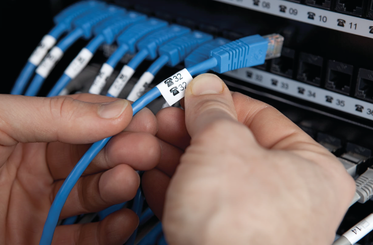 Hands connecting a blue Ethernet cable to a network switch.
