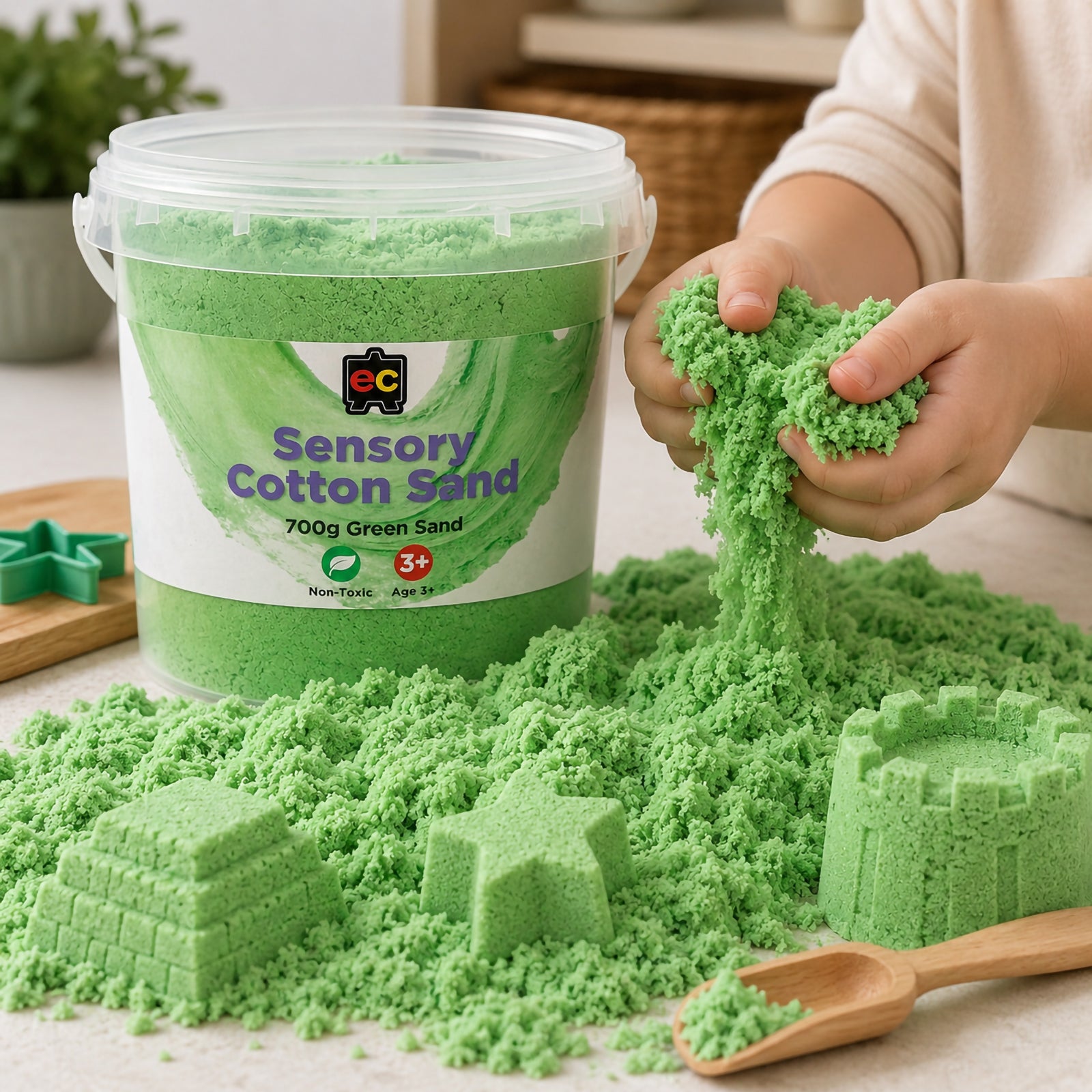 Child stretching and squeezing green sensory cotton sand beside moulded castles and reusable storage tub during sensory play.