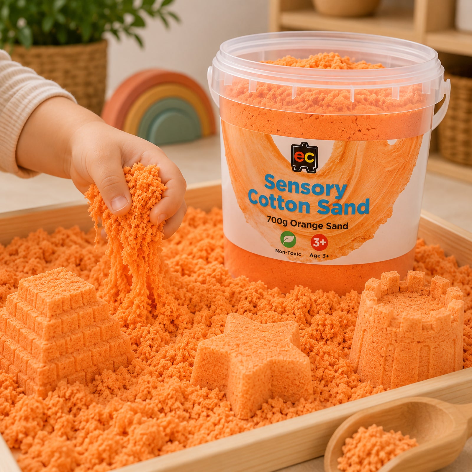 Child stretching and pouring vibrant orange sensory cotton sand while creating moulded shapes beside Educational Colours reusable storage tub.