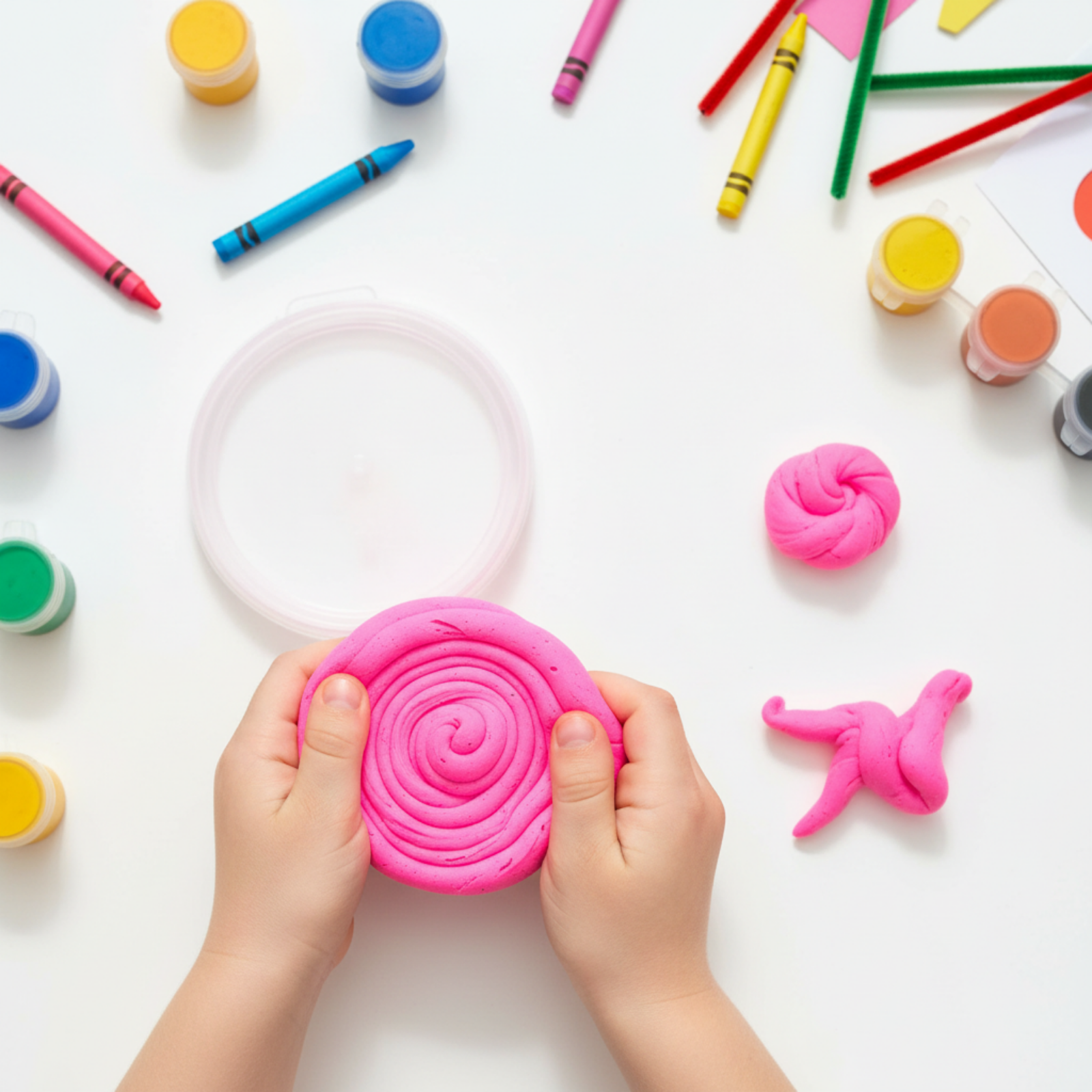 Overhead view of child holding swirled fluoro pink sensory dough surrounded by colourful art supplies and creative learning materials.