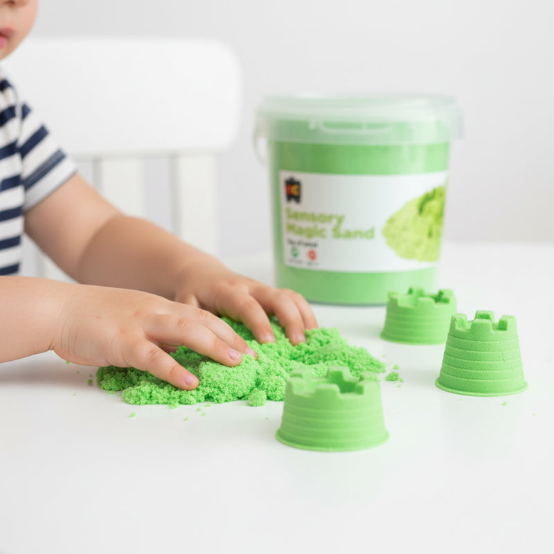 Young child exploring soft green sensory magic sand with castle moulds and reusable storage container during imaginative tactile play activity.