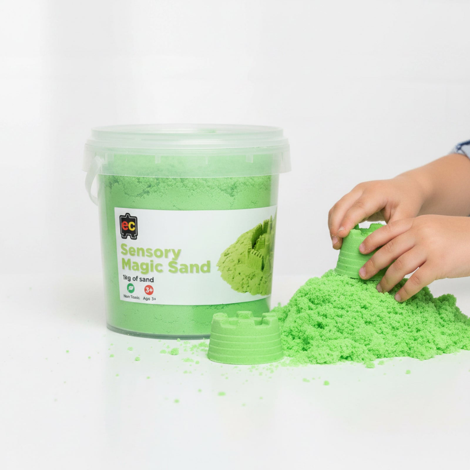 Child using green Educational Colours Sensory Magic Sand to shape small sand castles beside a large reusable 1kg storage tub on a clean play surface.