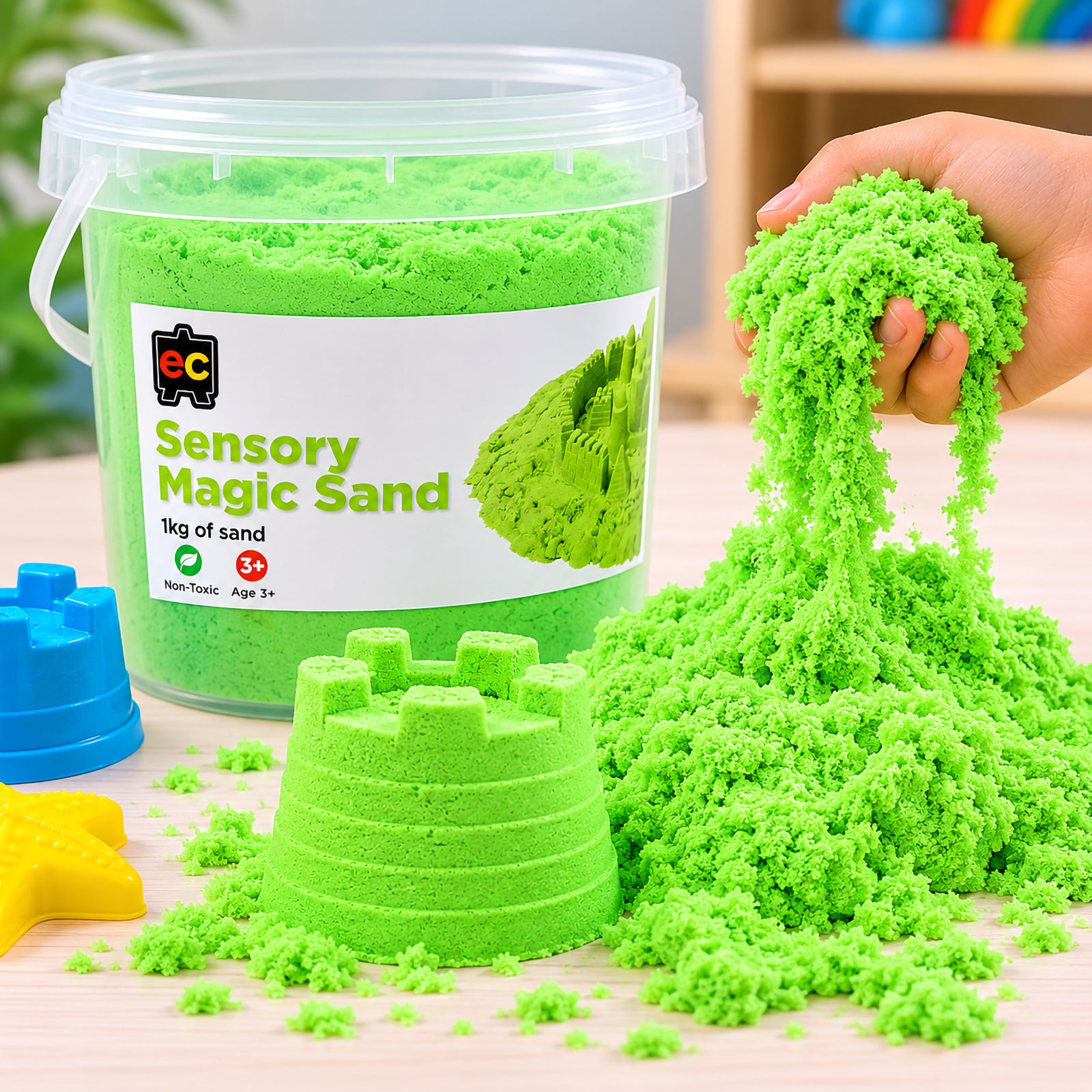 Close up of vibrant green sensory magic sand flowing through a child’s hand beside detailed castle moulds and Educational Colours 1kg sensory sand tub.