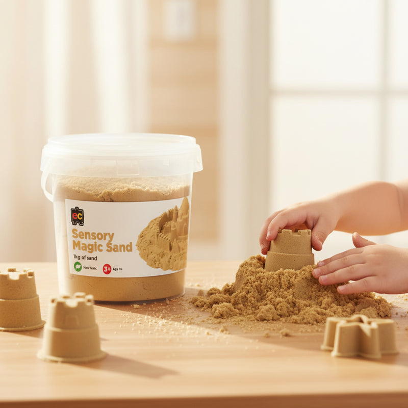 Young child shaping mouldable natural sensory sand into castle structures during hands on sensory play activity with reusable storage tub displayed nearby.