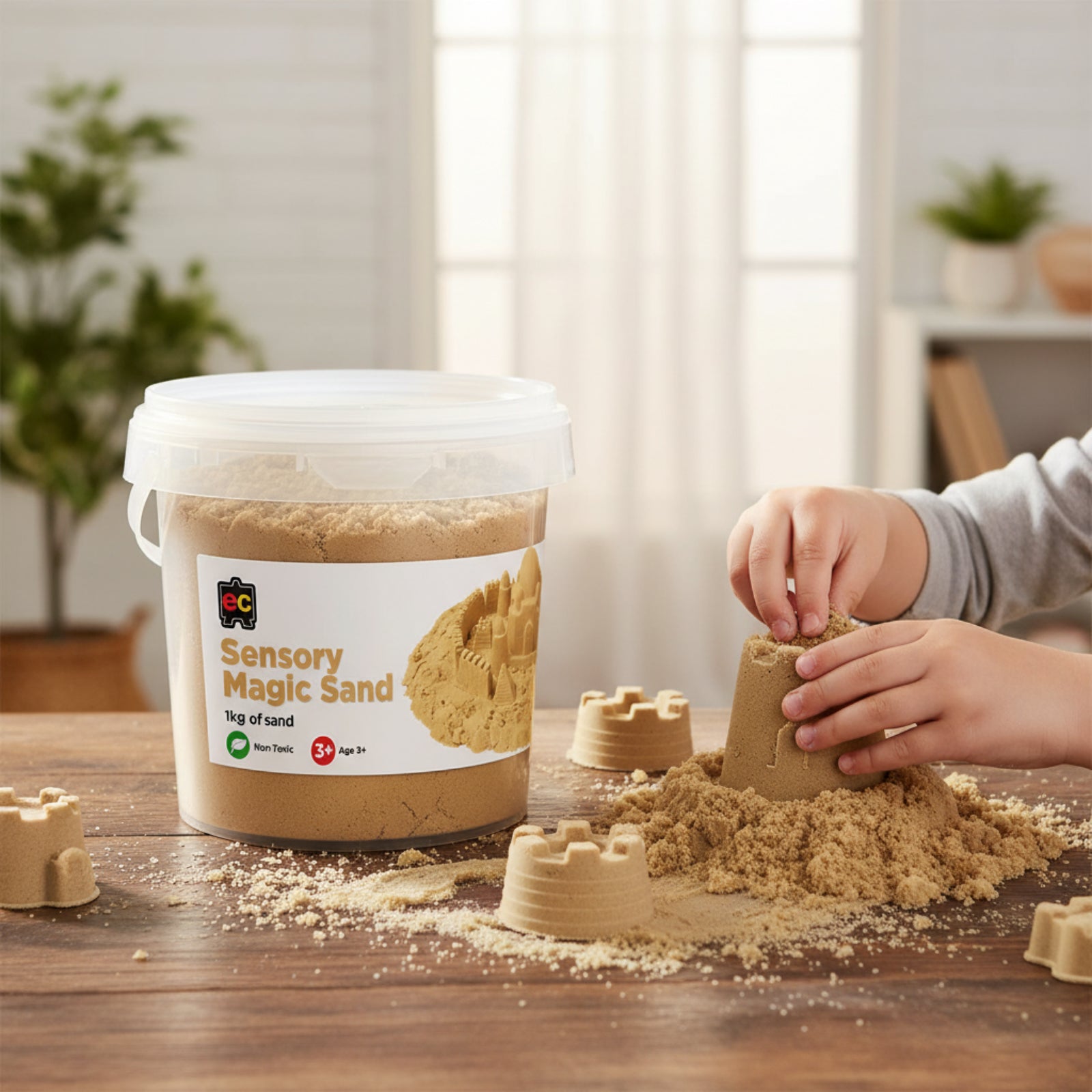 Child creating detailed sandcastle shapes using Educational Colours Sensory Magic Sand 1kg Natural on a wooden table beside the reusable storage tub in a bright indoor learning space.