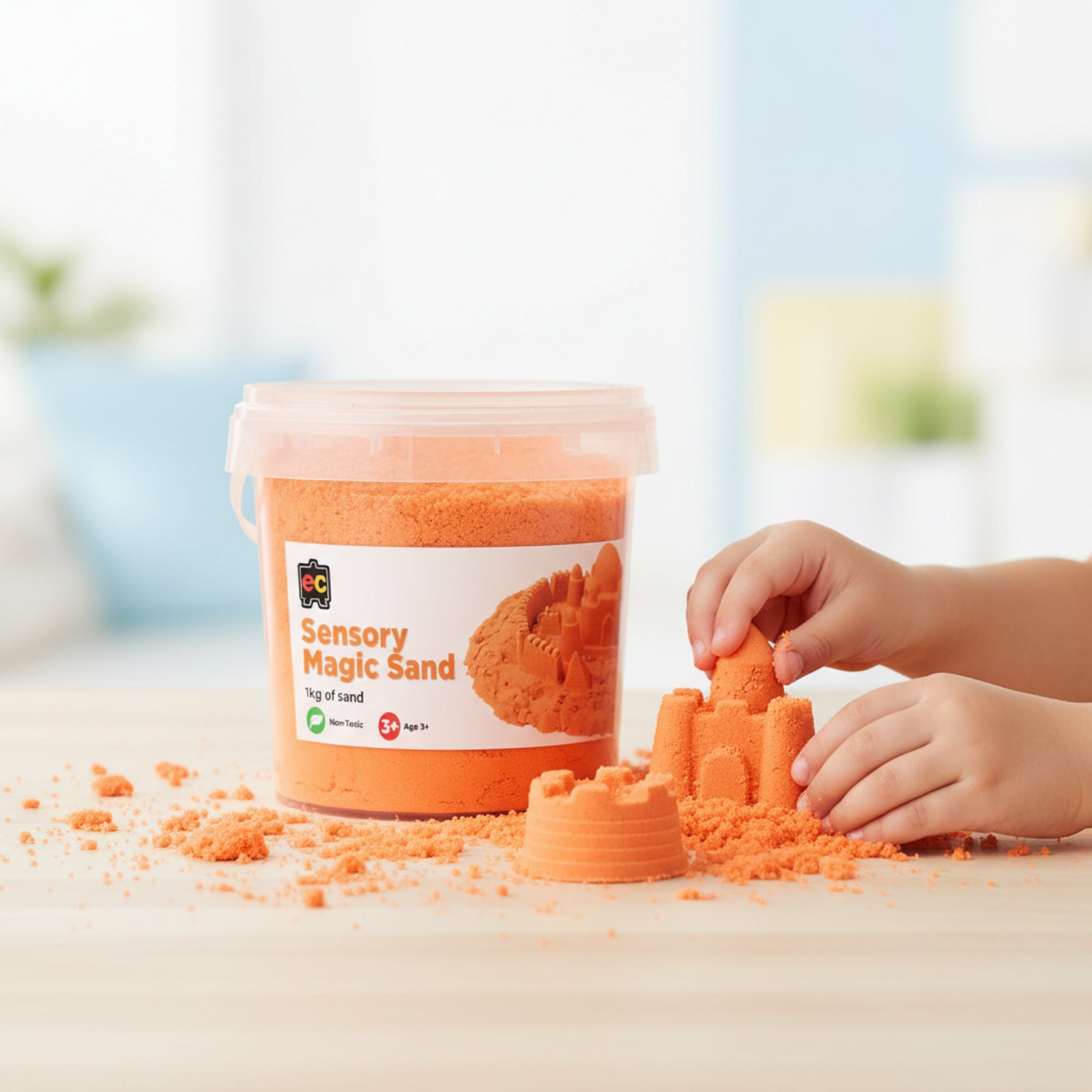 Child creating detailed sand castle shapes using Educational Colours Sensory Magic Sand 1kg Orange beside reusable storage tub on tabletop.