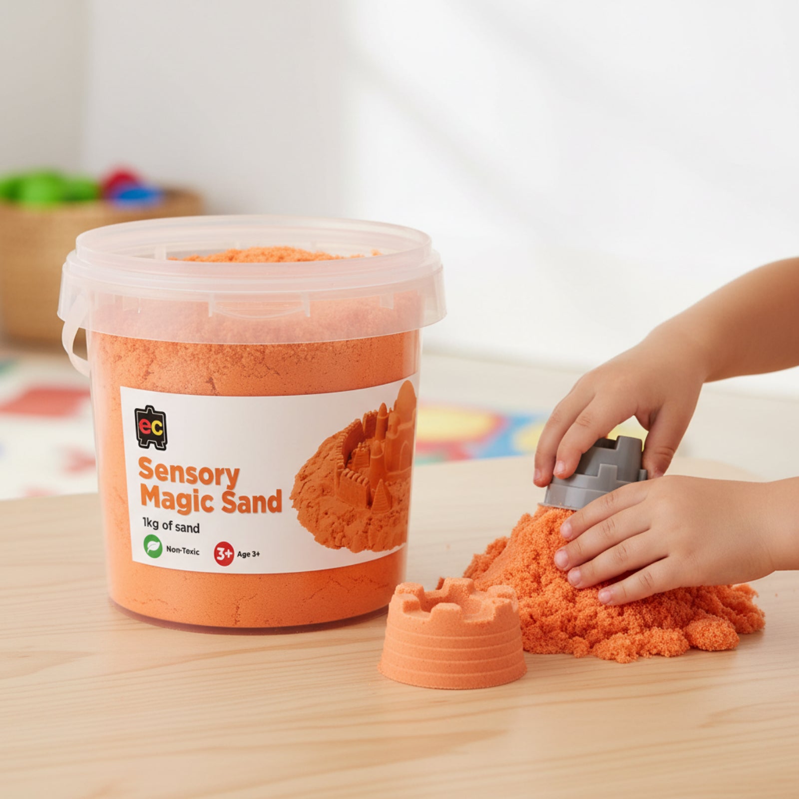 Young child using moulds with bright orange sensory magic sand during imaginative tactile play activity with reusable 1kg container nearby.